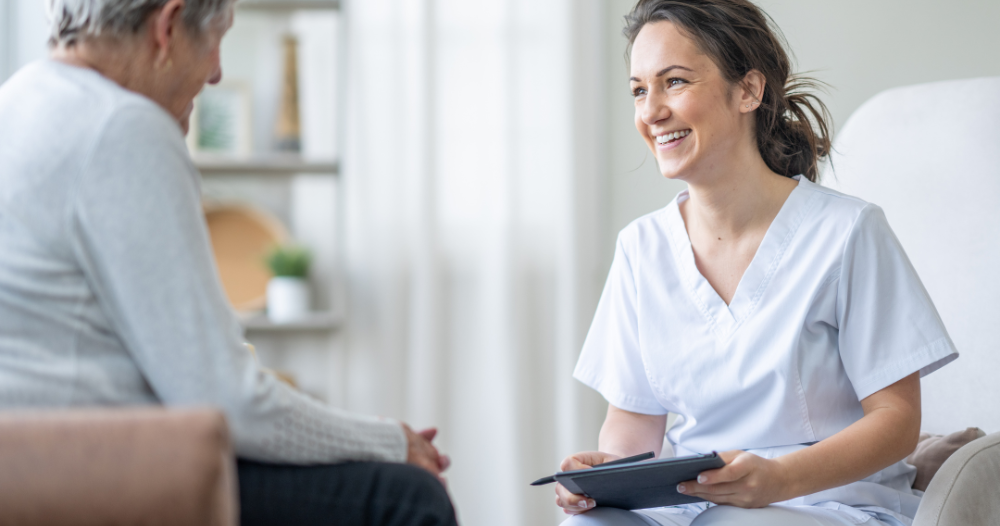 A woman smiles and enjoys her caregiving job as she writes notes down with a client.