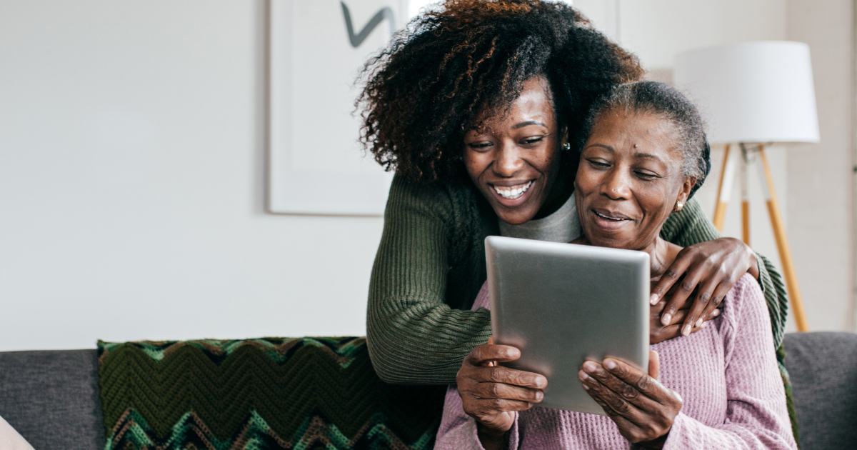 A caregiver helps a senior with her tablet, representing the rise of technology in home care.