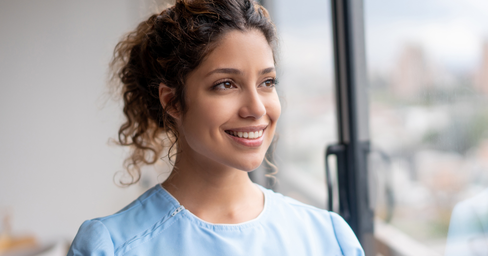 A woman in scrubs smiles, representing the satisfaction that can come with transitioning into a professional caregiving career.