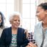 A caregiver talks with a client and her daughter, representing the type of communication that is vital when taking on a person-centered care approach.