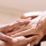 A pair of younger hands hold older ones, representing the compassionate care that a professional caregiver can provide.