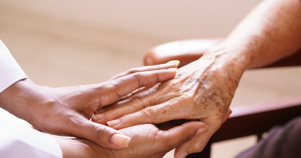 A pair of younger hands hold older ones, representing the compassionate care that a professional caregiver can provide.