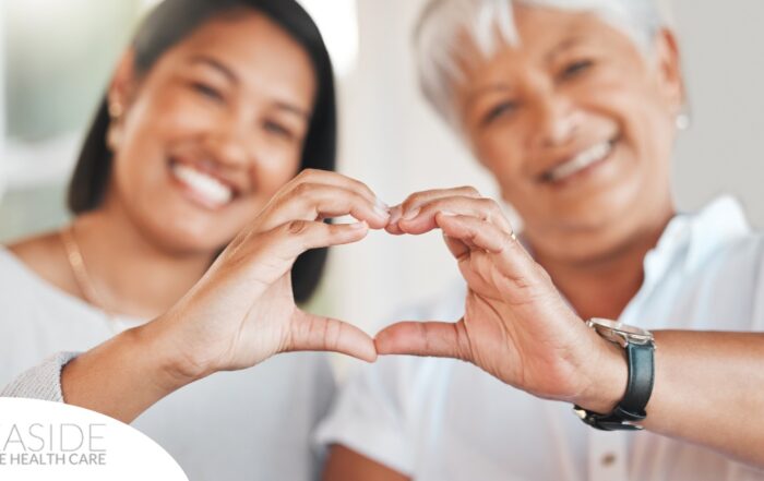 A daughter and an older mother create a heart with their hands, representing the feeling that is highlighted during National Family Caregivers Month