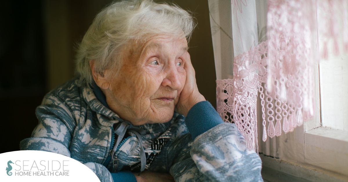 An older woman peacefully looks out of the window while the sun is still up, representing what can happen with sundowning.