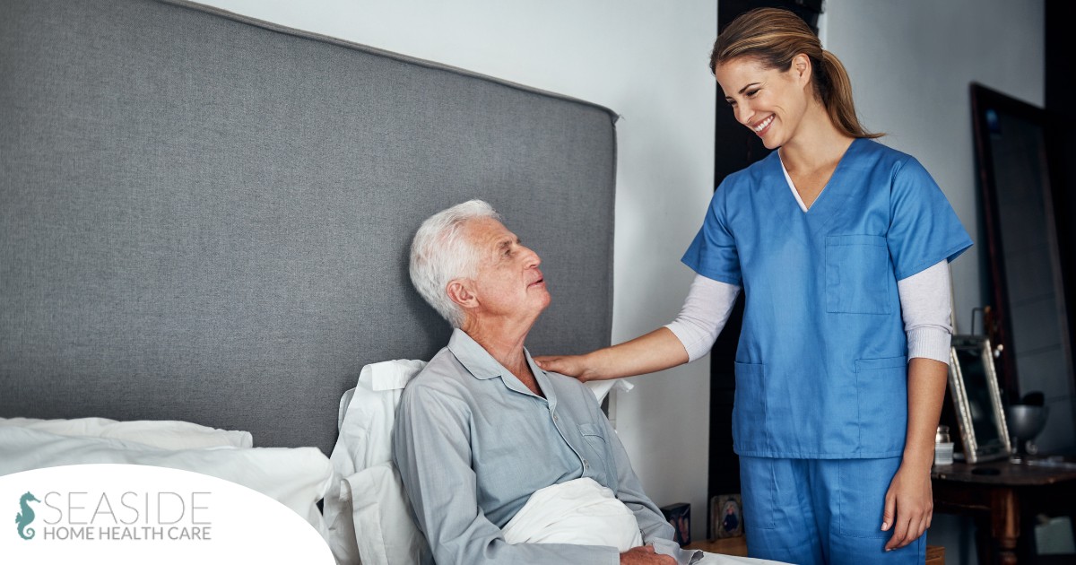 A caregiver smiles at an older client in bed, representing the compassion involved in being a live-in caregiver.