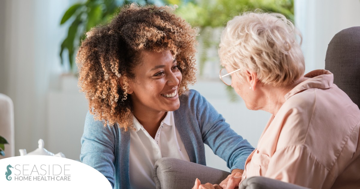 A caregiver smiles at an older client in a chair, representing the joy that can come from a healthy work-life balance.